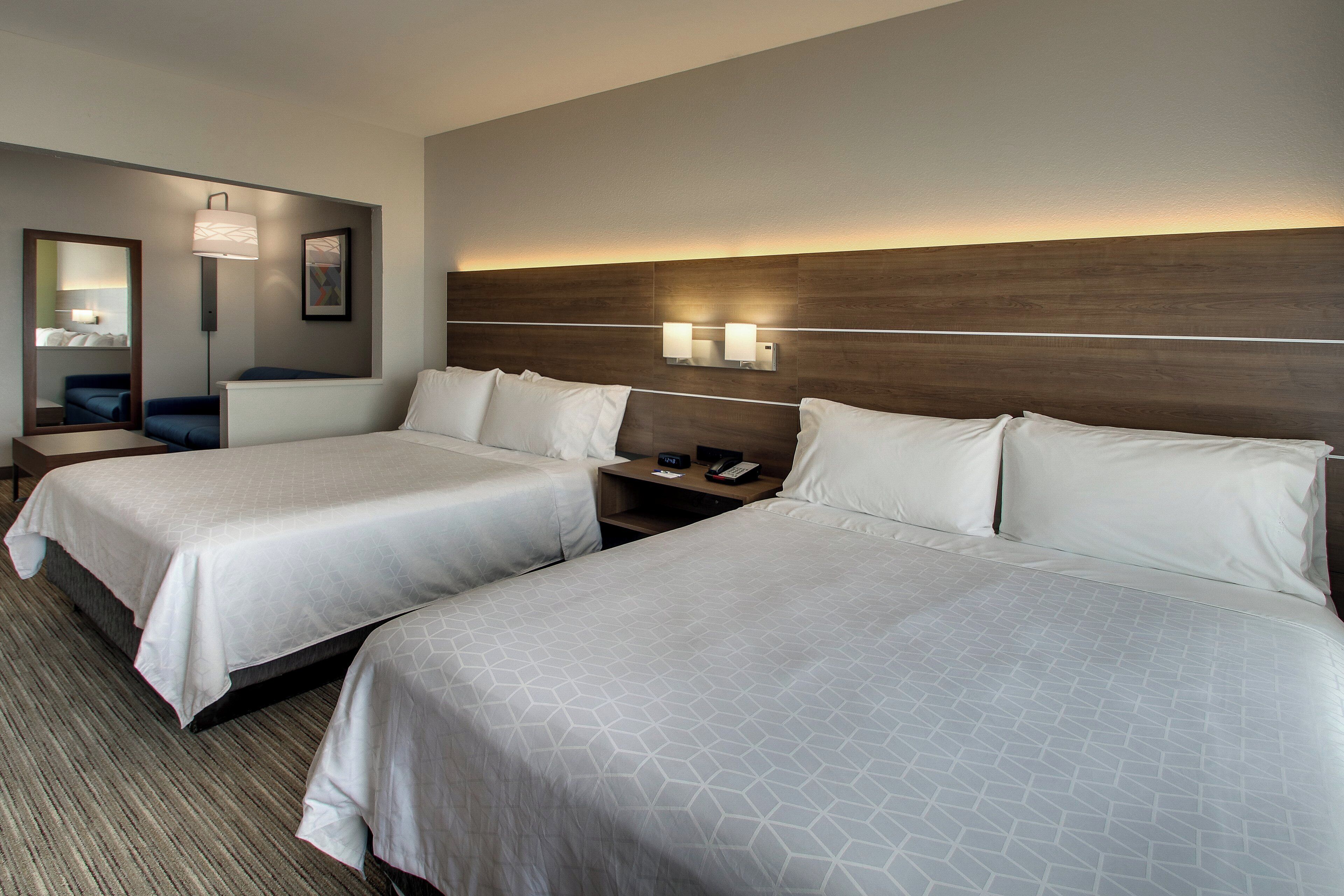 A hotel room with two beds, a nightstand, a lamp, and a mirror.
