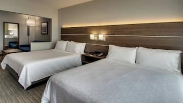 A hotel room with two beds, a nightstand, a lamp, and a mirror.