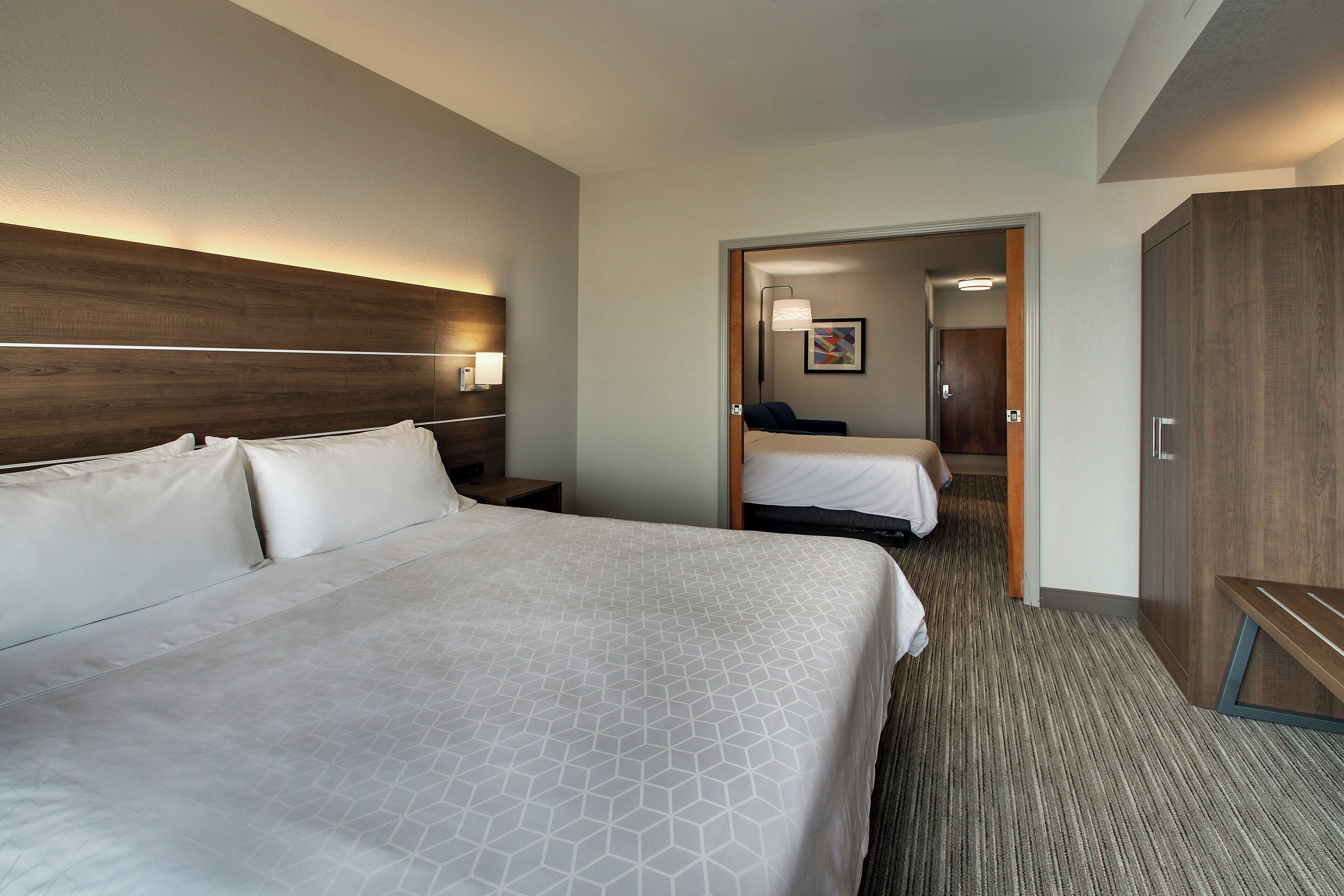 Een hotelkamer met een groot bed, een kleiner bed, een kledingkast en een nachtkastje met een lamp.