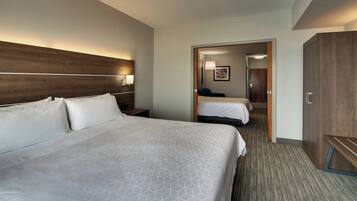 Een hotelkamer met een groot bed, een kleiner bed, een kledingkast en een nachtkastje met een lamp.