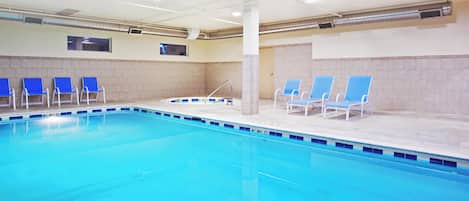 An indoor swimming pool with blue chairs and a tiled wall.
