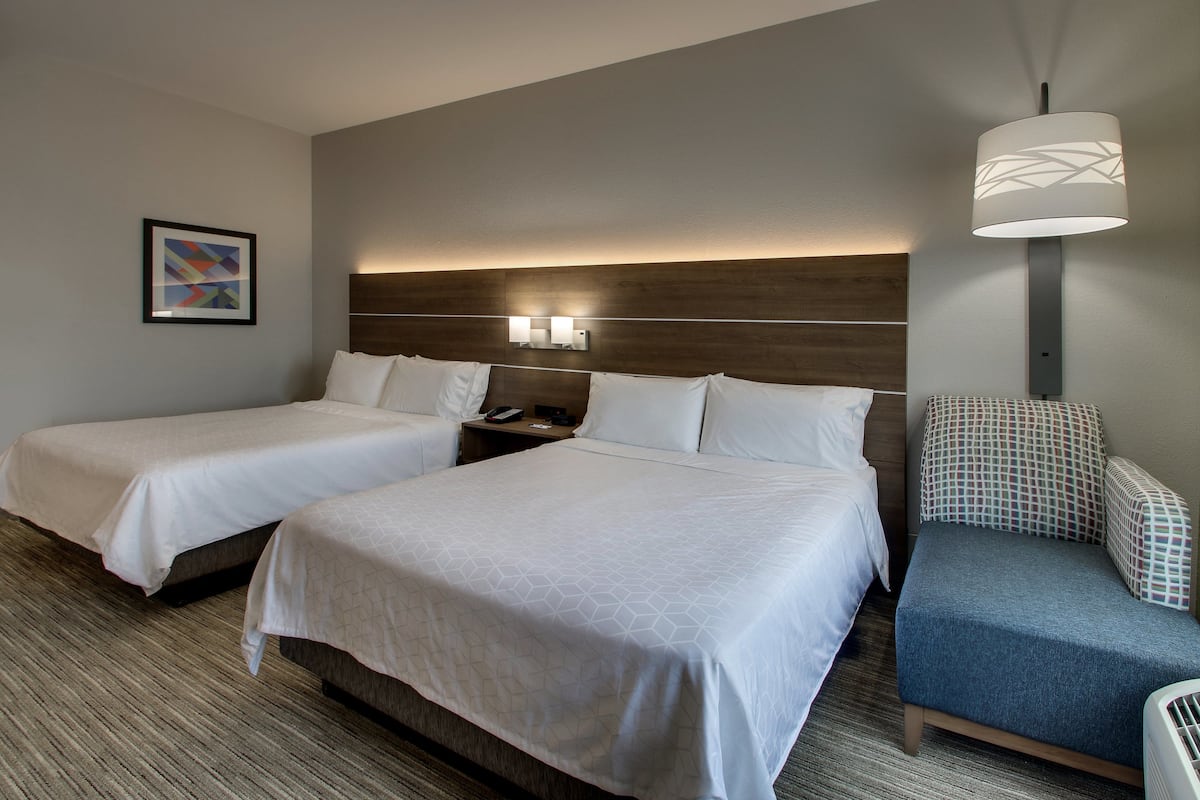 A hotel room with two beds, a nightstand, a lamp, and a chair.