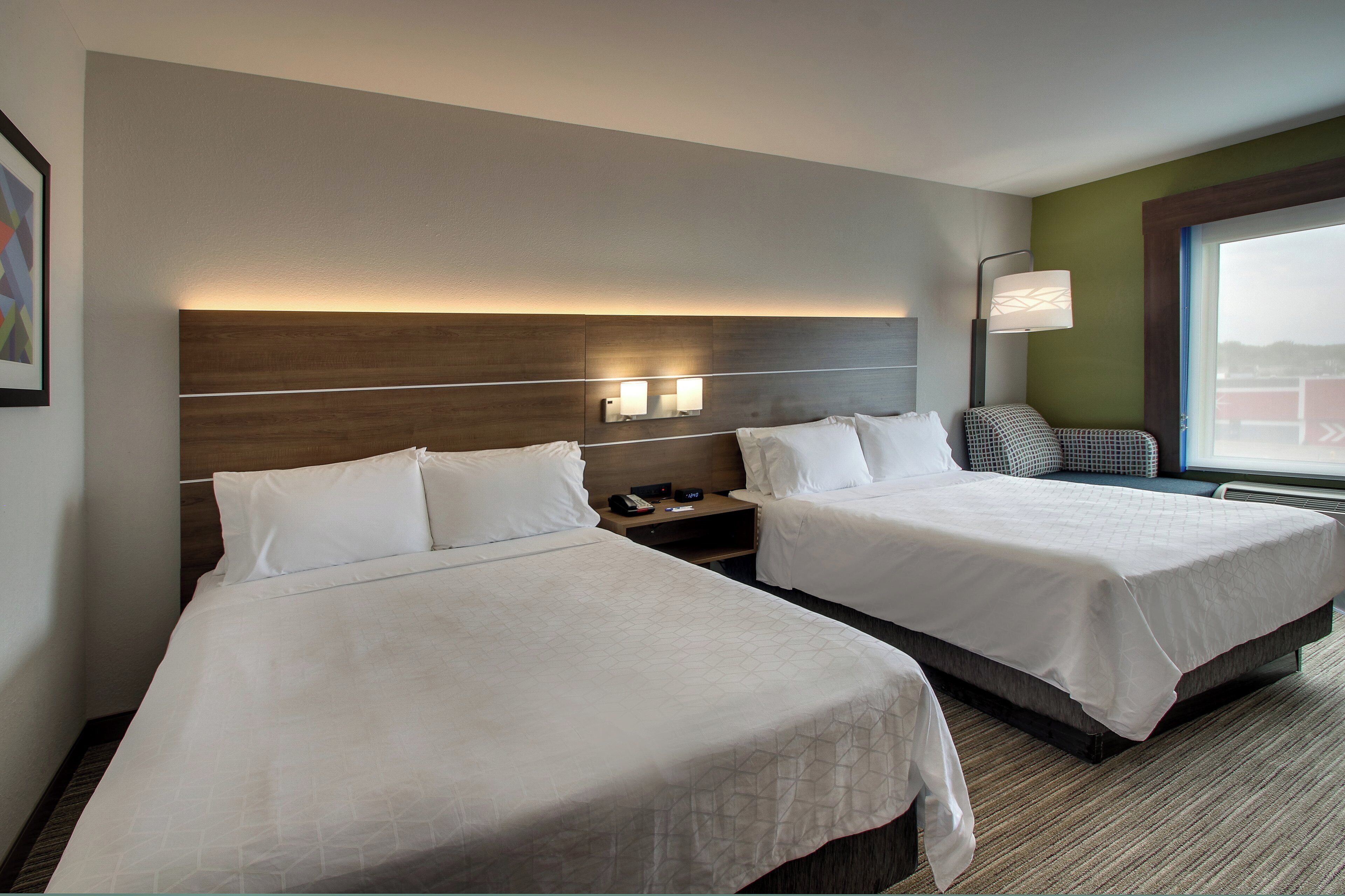 A hotel room with two beds, a nightstand, a lamp, and a window with a view.