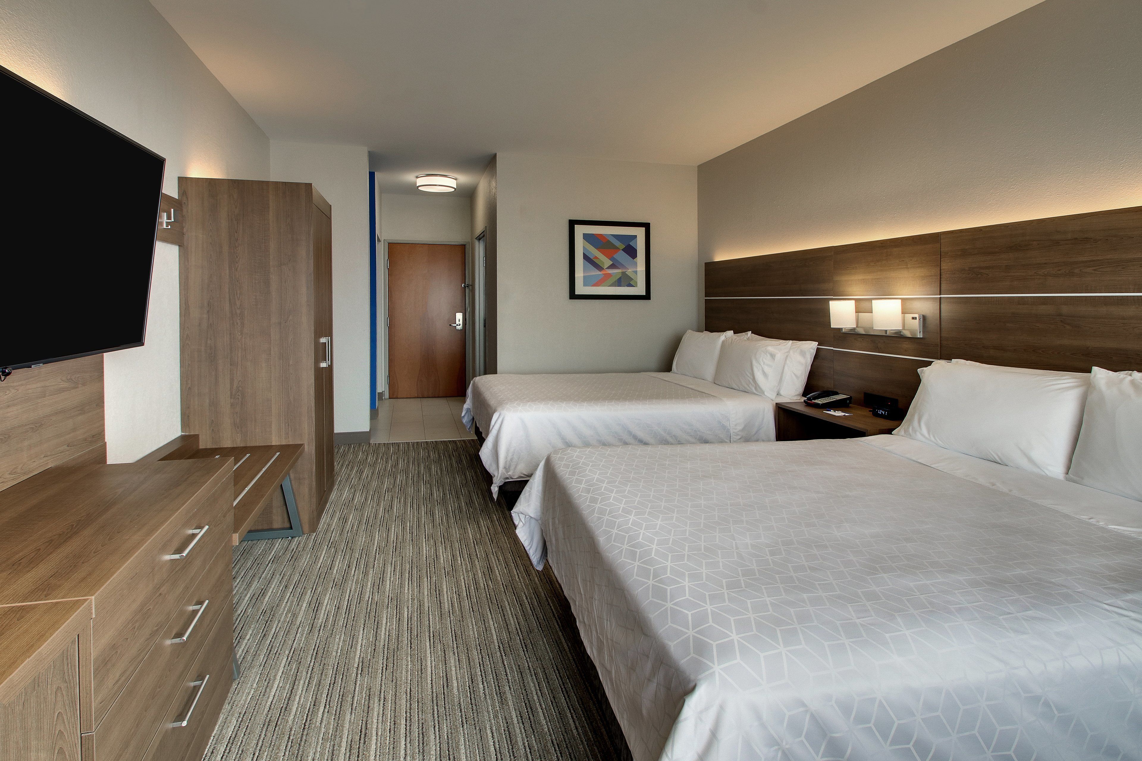 A hotel room with two beds, a TV, a wooden dresser, and a framed picture on the wall.