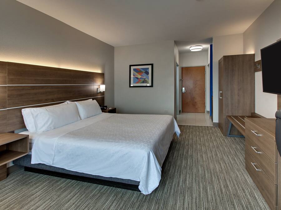 A modern hotel room with a large bed, bedside tables, a flat-screen TV, and a wooden wardrobe.