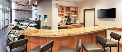A bar area with a granite countertop, bar stools, a coffee machine, and shelves stocked with bottles.