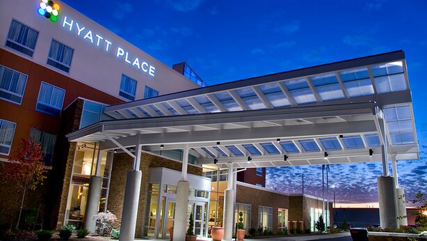 Een Hyatt Place hotel met een overdekte ingang, grote ramen en een aangelegde omgeving met plantenpotten.