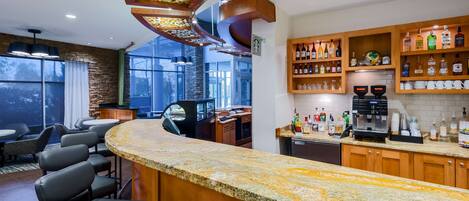 A bar area with a granite countertop, bar stools, and a variety of liquor bottles.