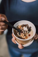 Una persona sosteniendo un tazón de avena con pasas y una cuchara.