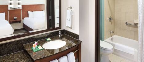 A hotel bathroom with a large mirror, a sink, a toilet, and a shower area.