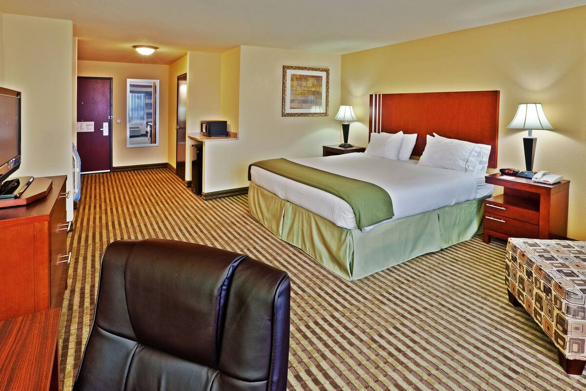 A hotel room with a large bed, a desk, a chair, a TV, and a lamp.
