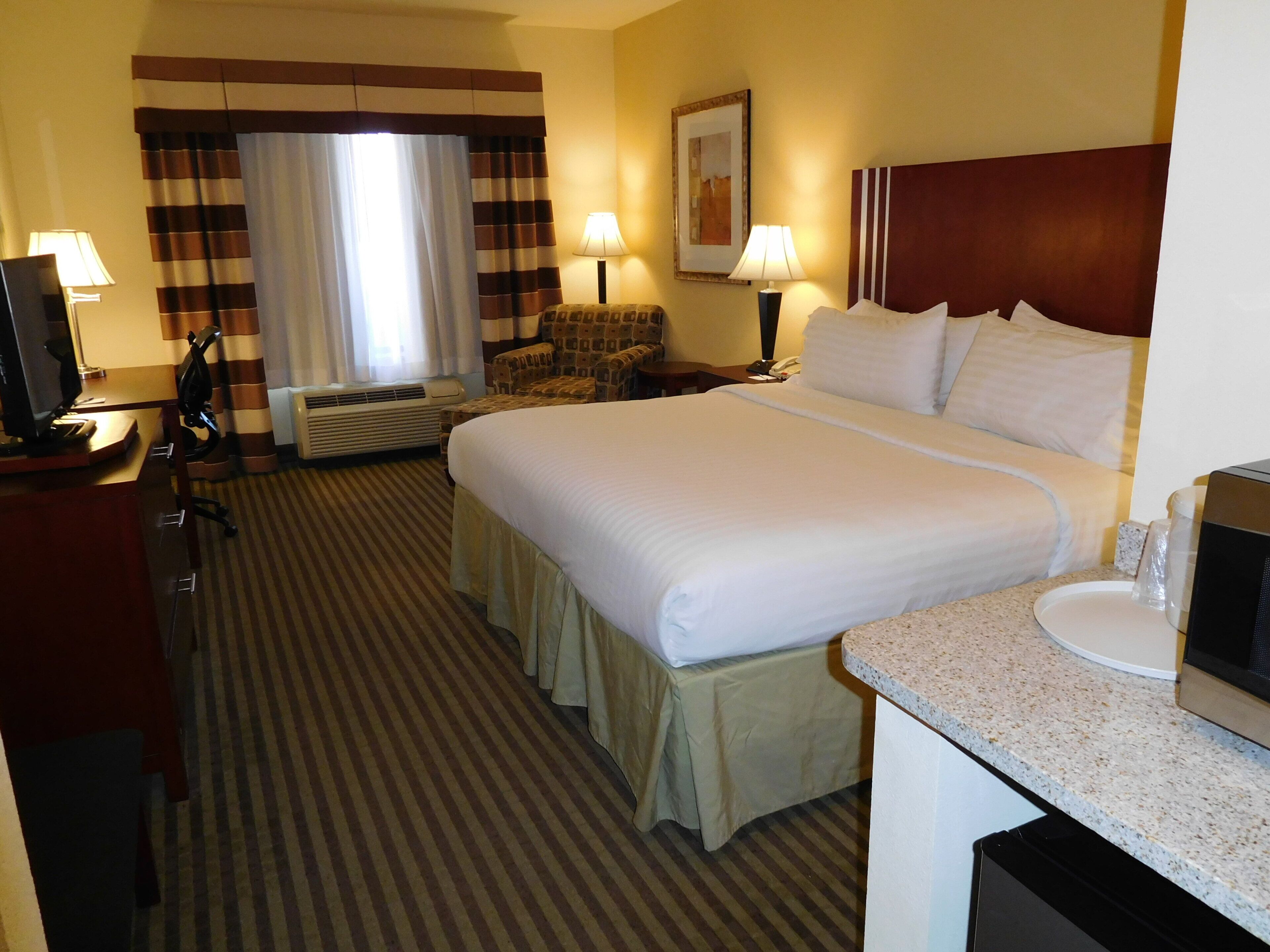 A hotel room with a large bed, a desk with a computer, a chair, a sofa, a lamp, and a picture on the wall.
