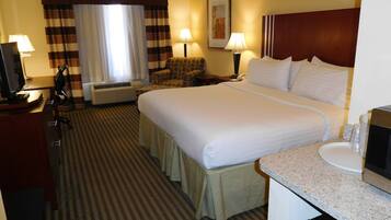 A hotel room with a large bed, a desk with a computer, a chair, a sofa, a lamp, and a picture on the wall.