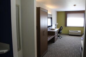 Quarto de hotel com escrivaninha, cadeira e uma janela grande.
