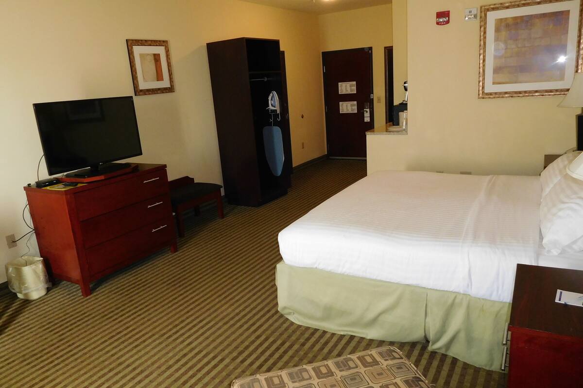 A hotel room with a bed, a television on a dresser, a wardrobe, and a desk with a chair.