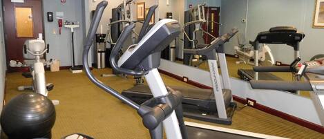 A gym with cardio machines, a mirror, and exercise balls.