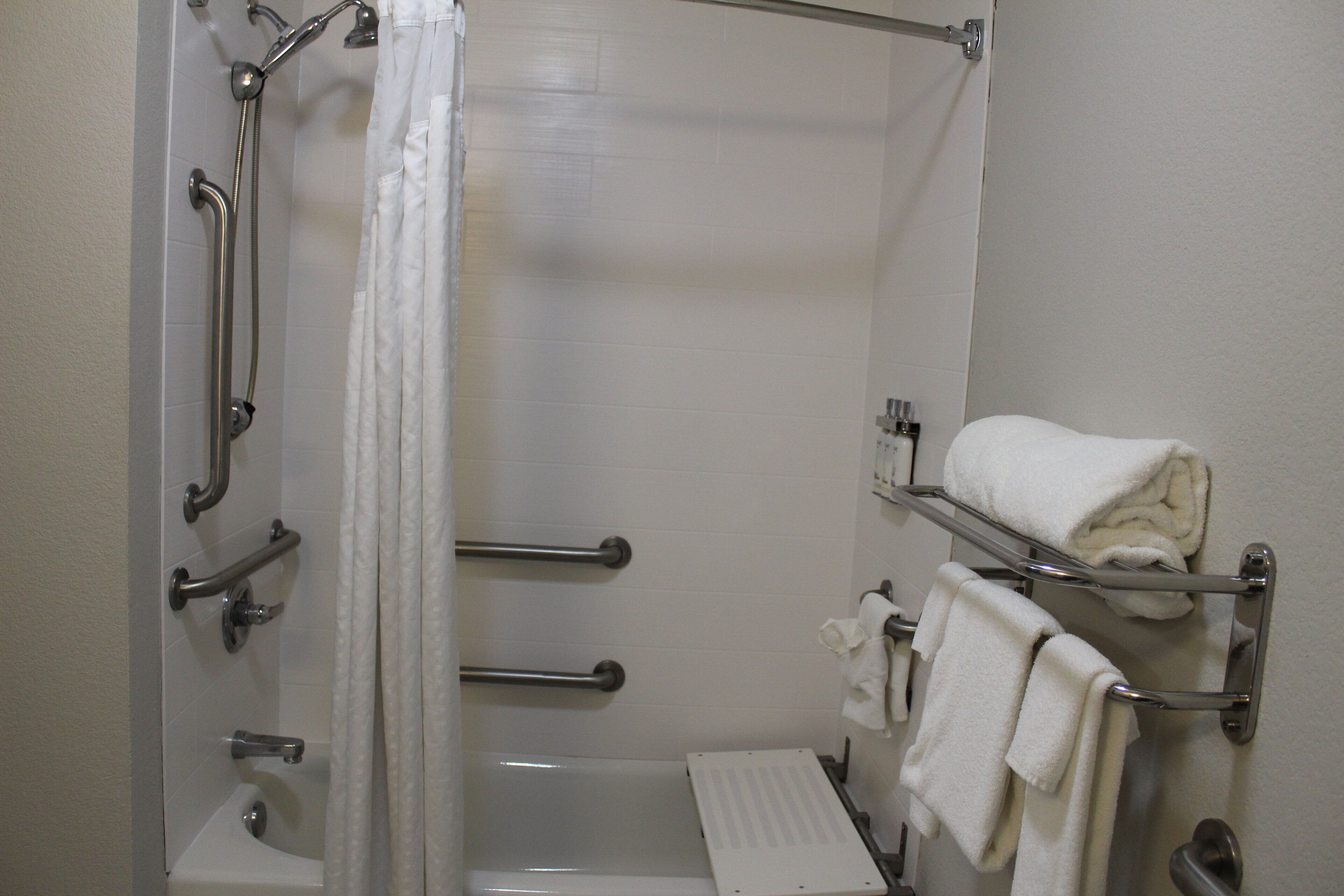 A bathroom with a shower, grab bars, a towel rack, and a toilet.