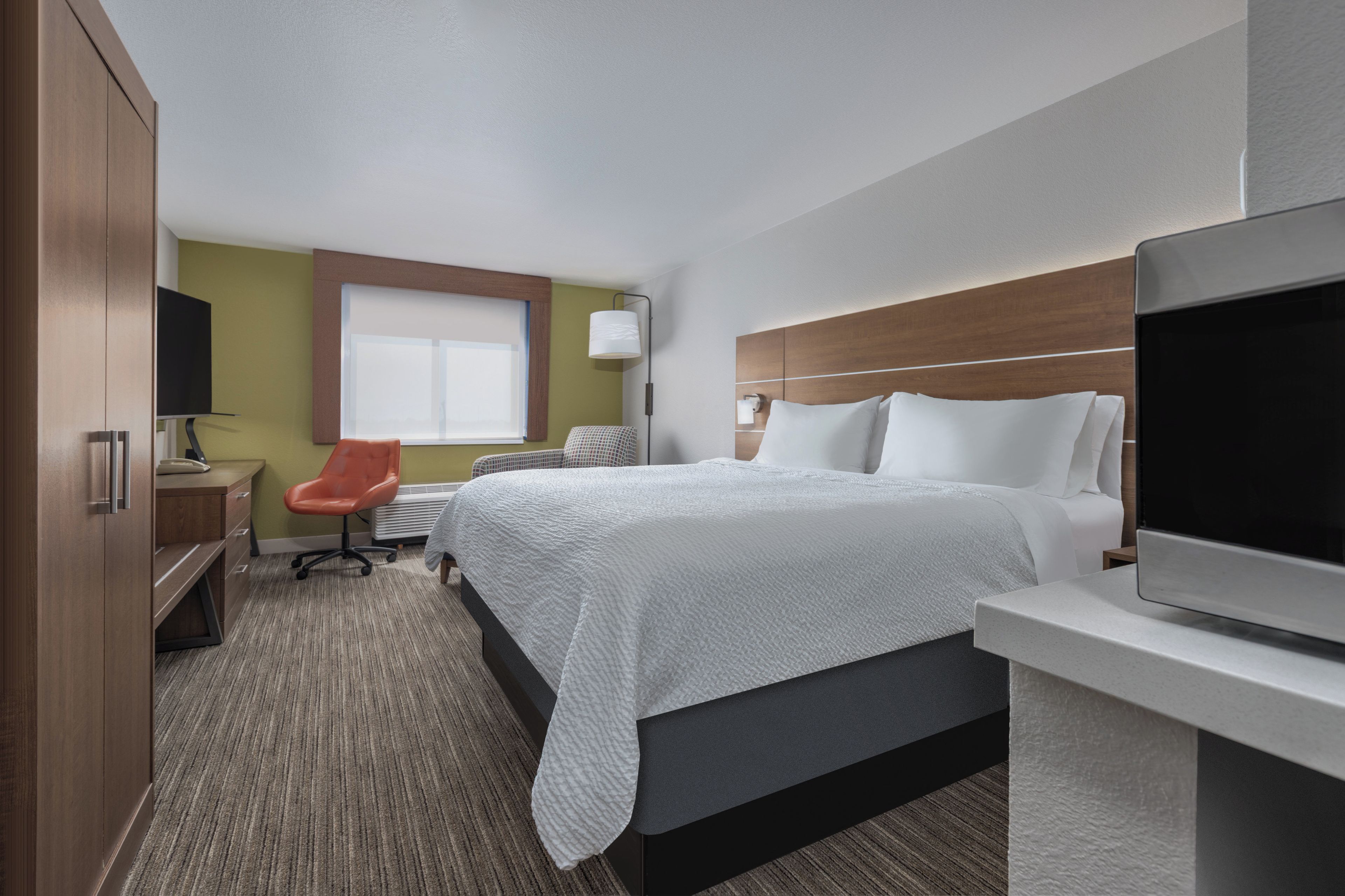 A hotel room with a bed, a desk, a chair, a television, and a window.