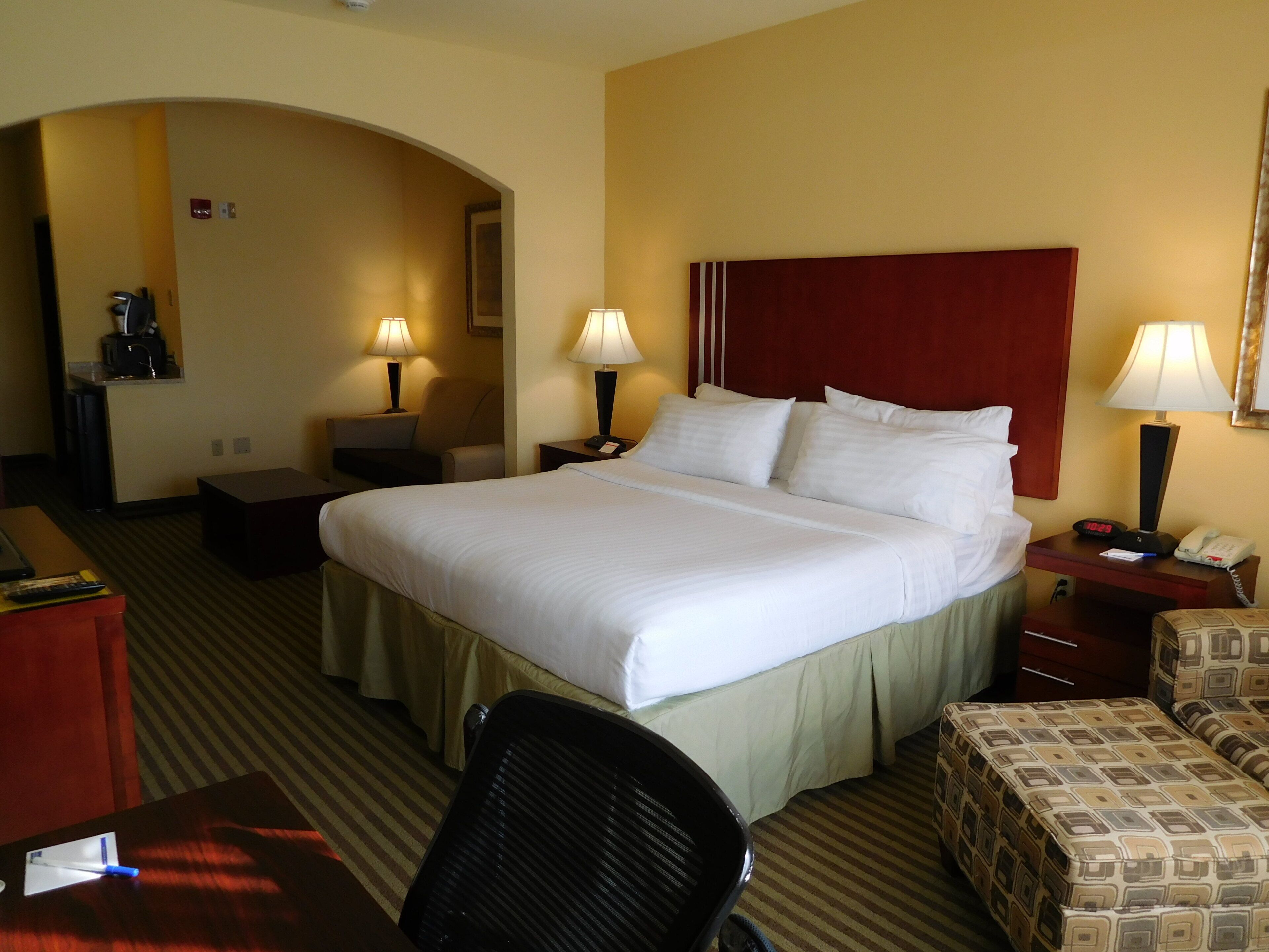 A hotel room with a large bed, two bedside tables with lamps, a desk, a chair, and a small sofa.