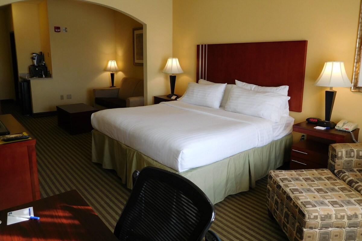 Habitación de hotel con una cama grande, dos mesitas de noche con lámparas, un escritorio, una silla y un pequeño sofá.
