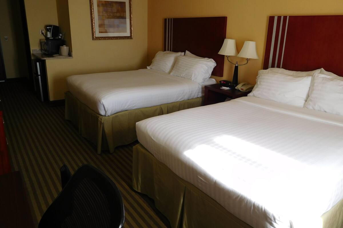 A hotel room with two beds, a desk with a coffee maker, a framed picture on the wall, and a lamp on the nightstand.