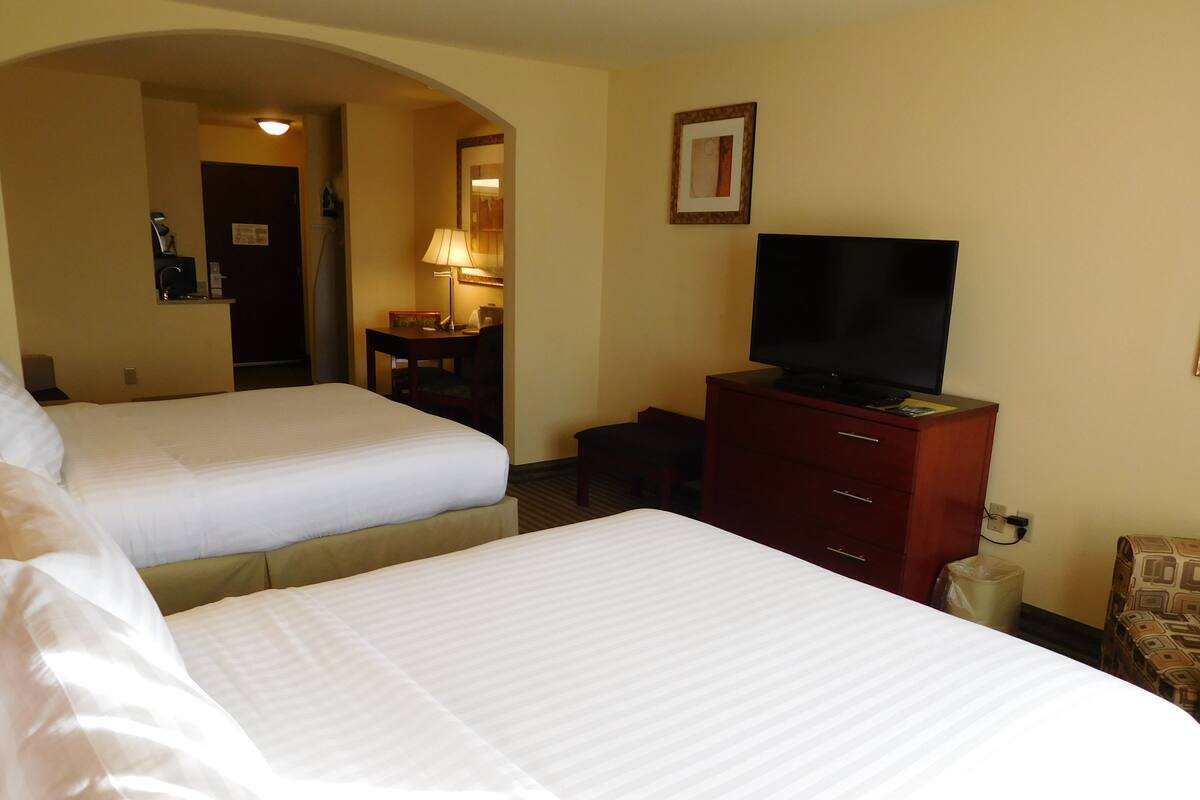 A hotel room with two beds, a TV on a dresser, and a desk with a lamp.
