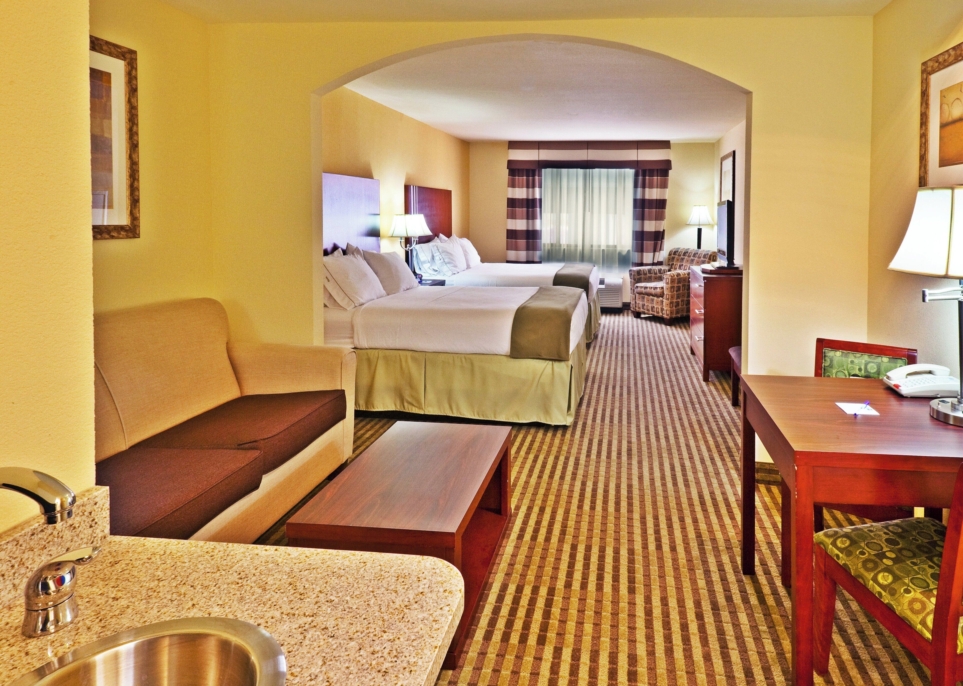 A hotel room with a bed, a sofa, a desk, a chair, a lamp, and a telephone.