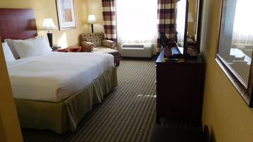A hotel room with a large bed, a desk, a chair, a television, and an air conditioning unit.