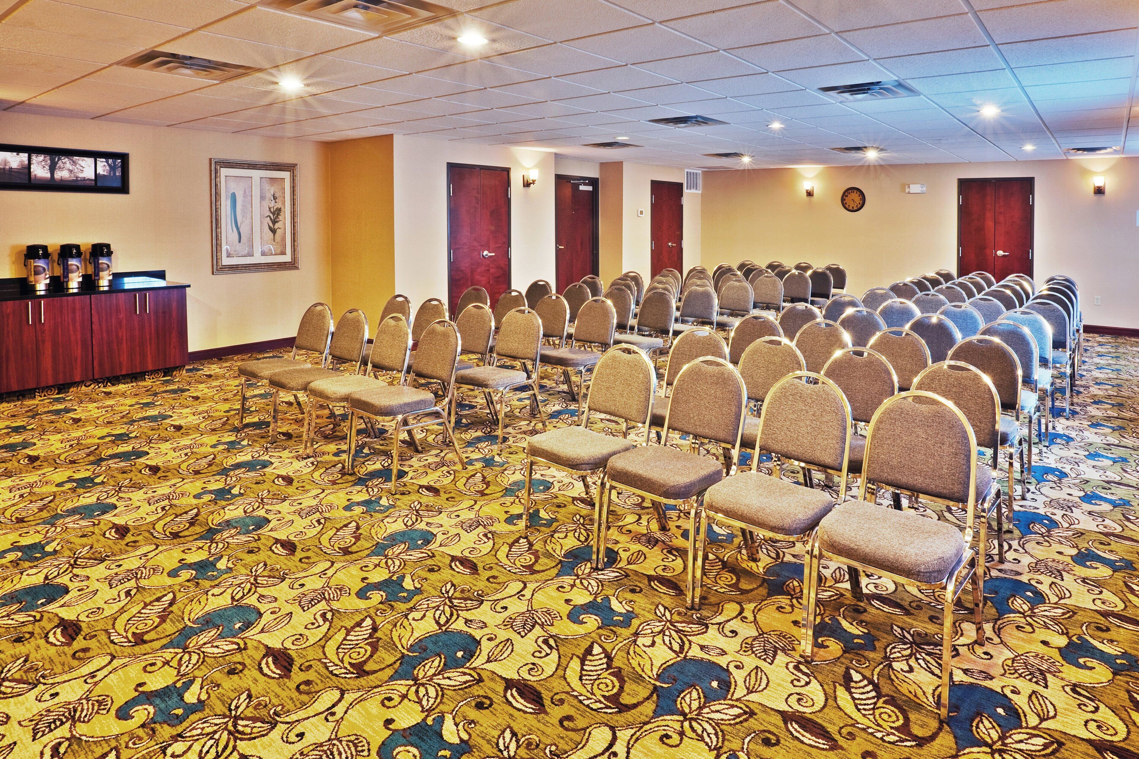 Un salón de conferencias con filas de sillas, un atril y una alfombra estampada.