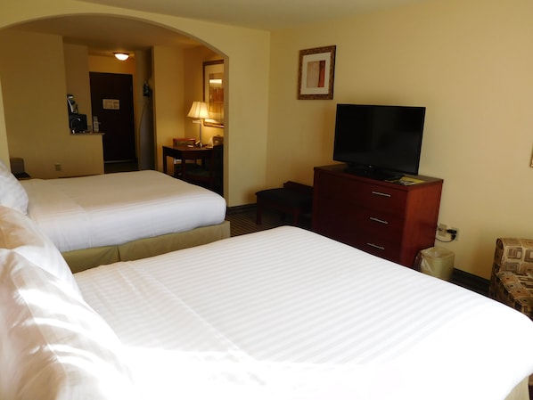 Quarto de hotel com duas camas, uma televisão sobre uma cômoda e uma escrivaninha com abajur.