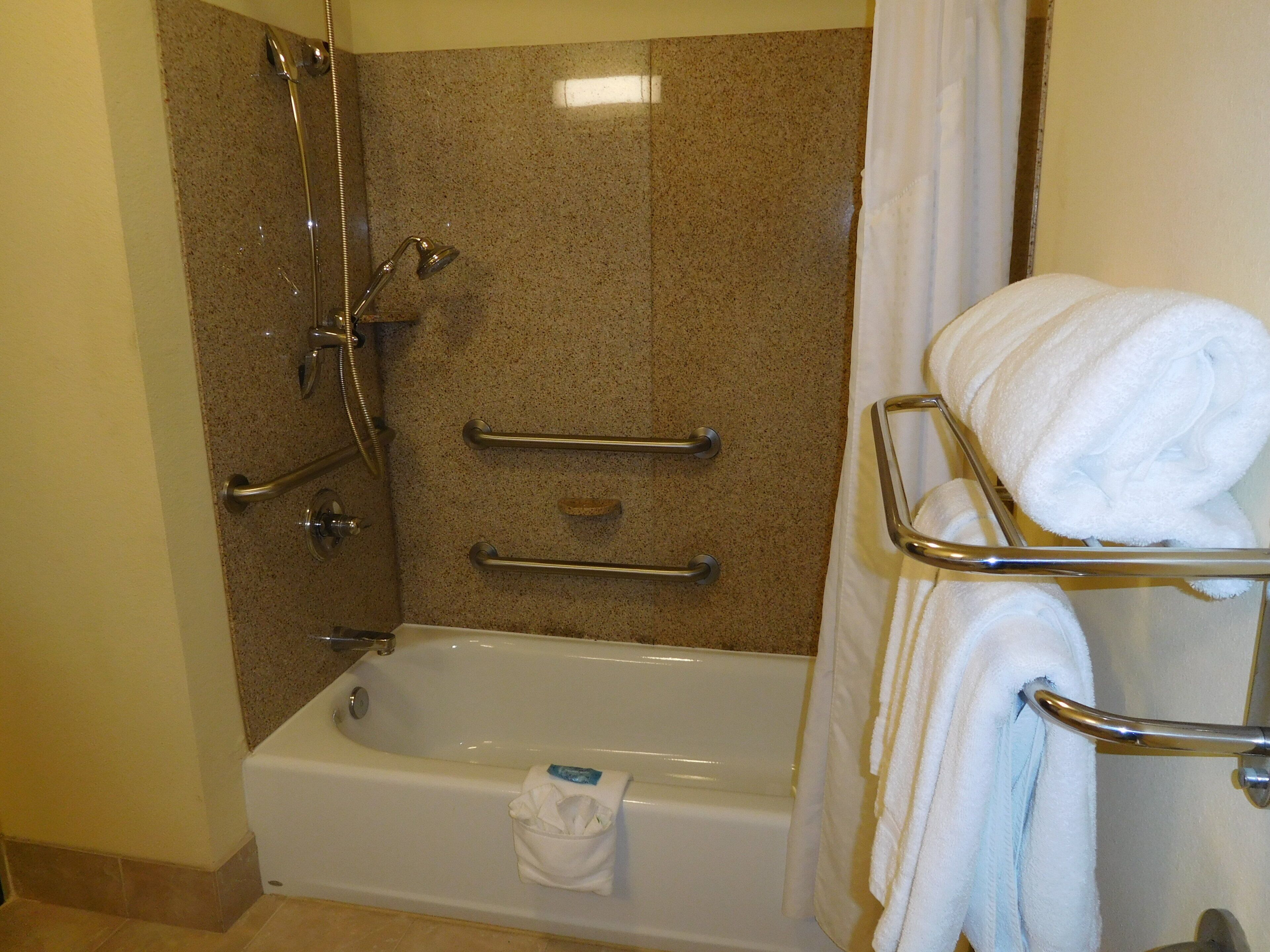 A bathroom with a bathtub, shower, grab bars, and a towel rack.