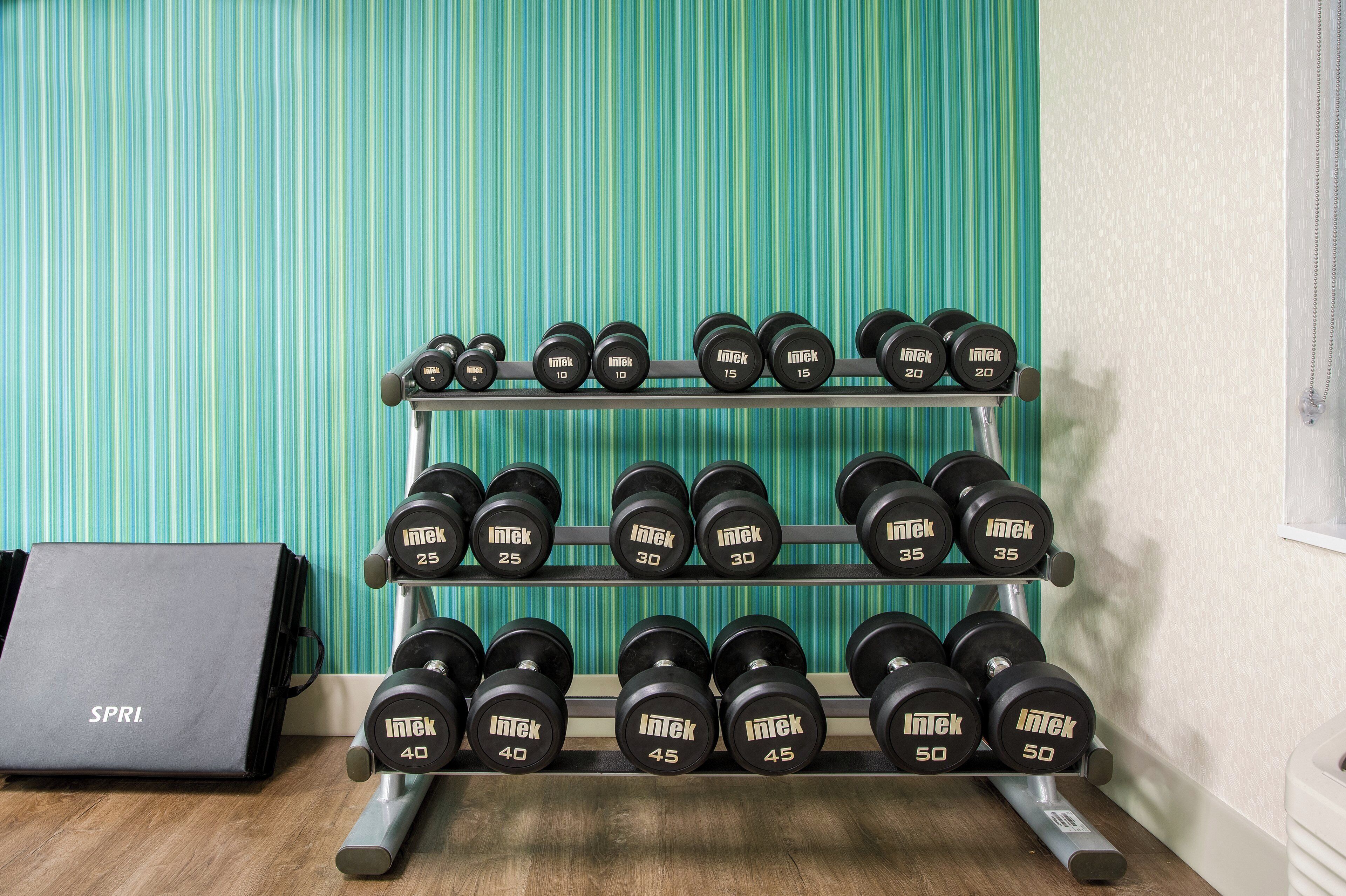 A set of dumbbells on a rack with a green striped wall in the background.