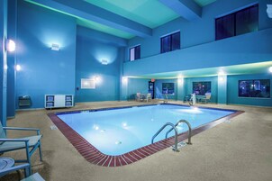 Piscina com borda de tijolos vermelhos, cercada por paredes azuis e um teto com iluminação embutida.