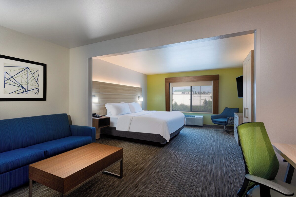 Una habitación de hotel con una cama, un sofá azul, una mesa de centro de madera, un escritorio y una silla.
