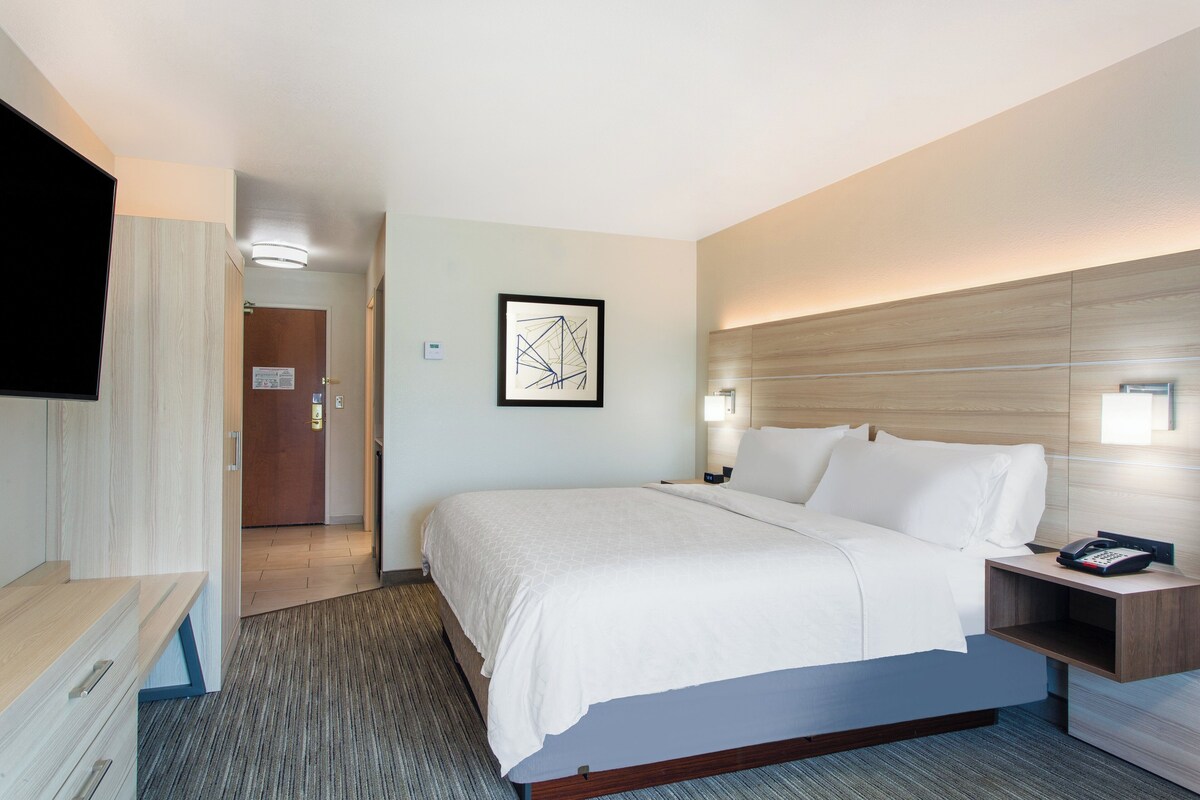 Una habitación de hotel con una cama, mesita de noche, lámpara y un cuadro en la pared.