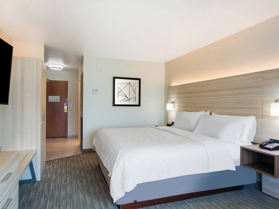 A hotel room with a bed, bedside table, lamp, and a painting on the wall.