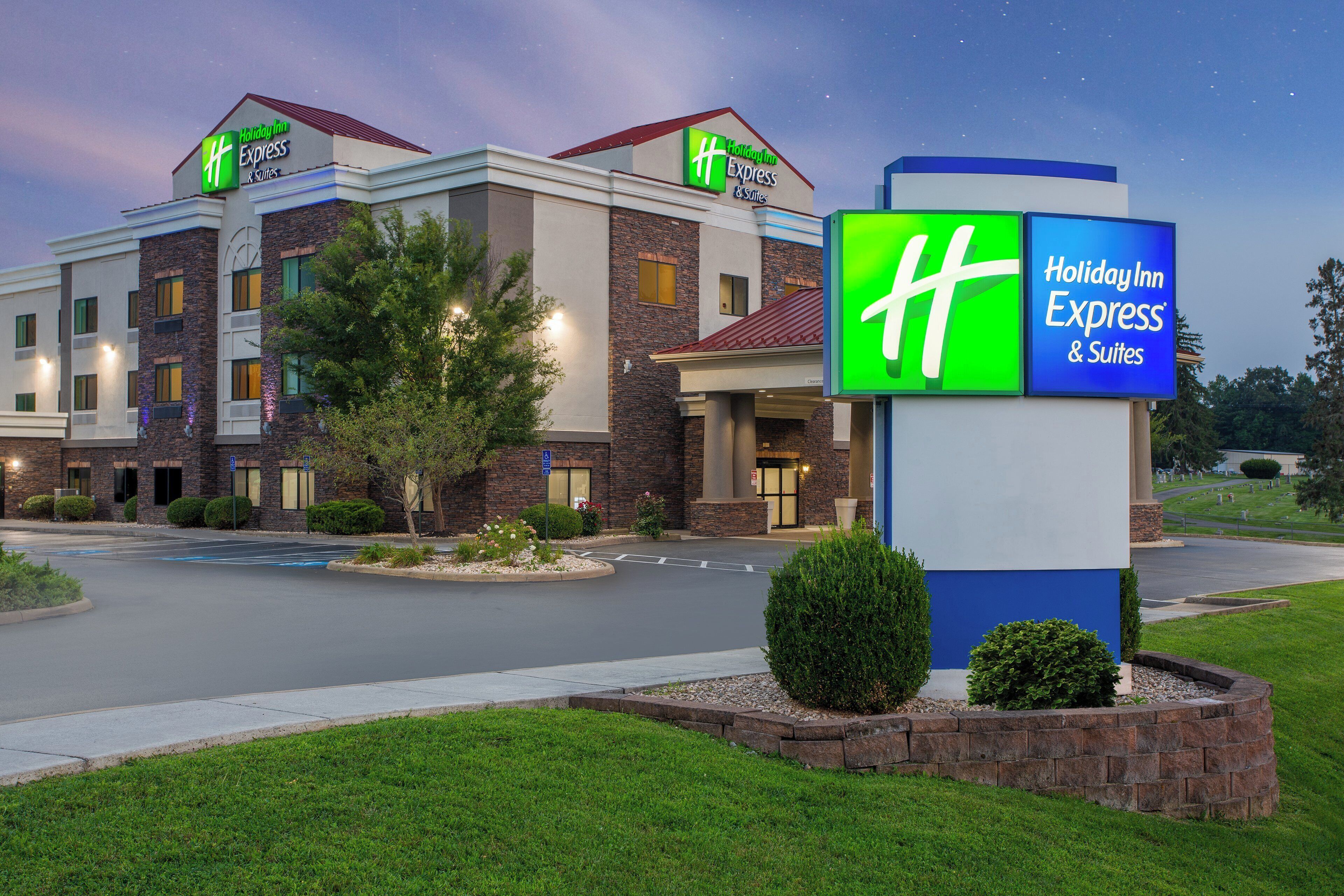 A Holiday Inn Express & Suites hotel with a brick facade, a well-maintained lawn, and a clear sky.