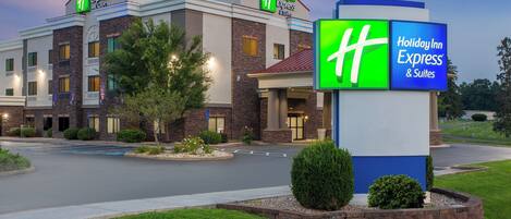 A Holiday Inn Express & Suites hotel with a brick facade, a well-maintained lawn, and a clear sky.