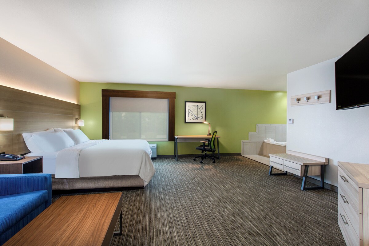 Una habitación de hotel con cama, escritorio, silla, televisor y un sofá azul.