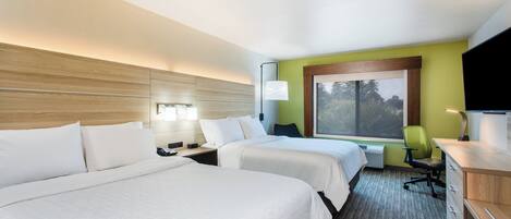 A hotel room with two beds, a desk, a chair, a window, and a lamp.