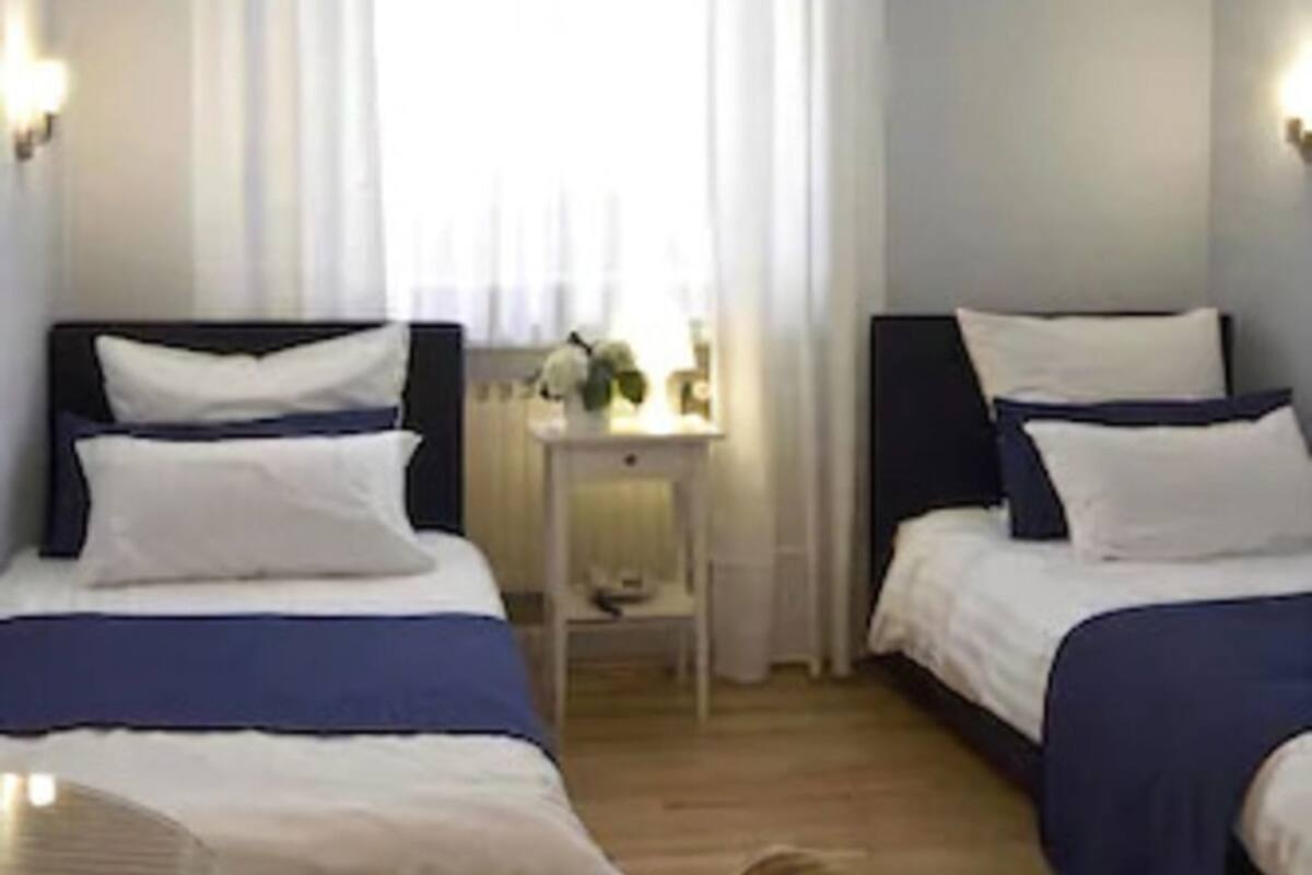 Ein Hotelzimmer mit zwei Betten, einem kleinen Tisch, einem Stuhl und einem Fenster mit Vorhängen.