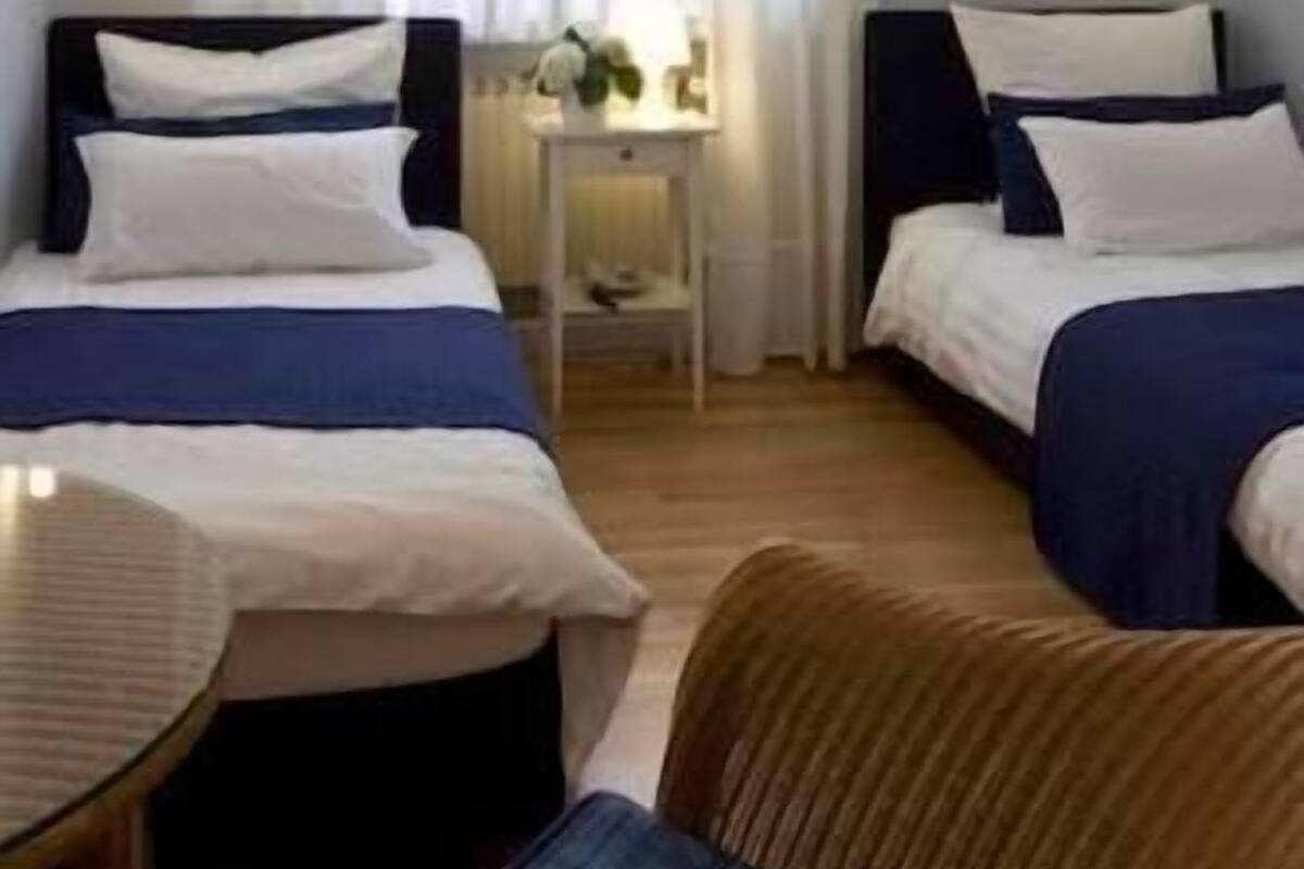 Ein Hotelzimmer mit zwei Betten, einem kleinen Tisch, einem Stuhl und einem Fenster mit Vorhängen.