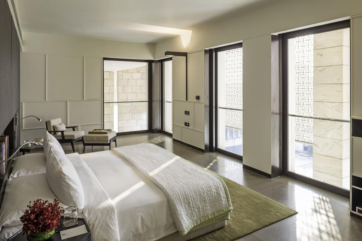 A modern hotel room with a large bed, a desk, and a chair. There are large windows with a view of the city.