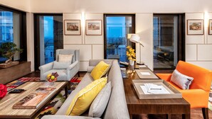 A modern living room with a sofa, armchairs, and a coffee table. There are framed pictures on the walls and a potted plant.