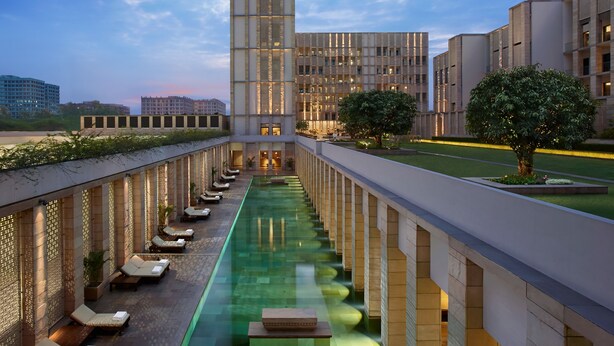 A hotel with a central pool, lounge chairs, and a modern building with a glass facade.