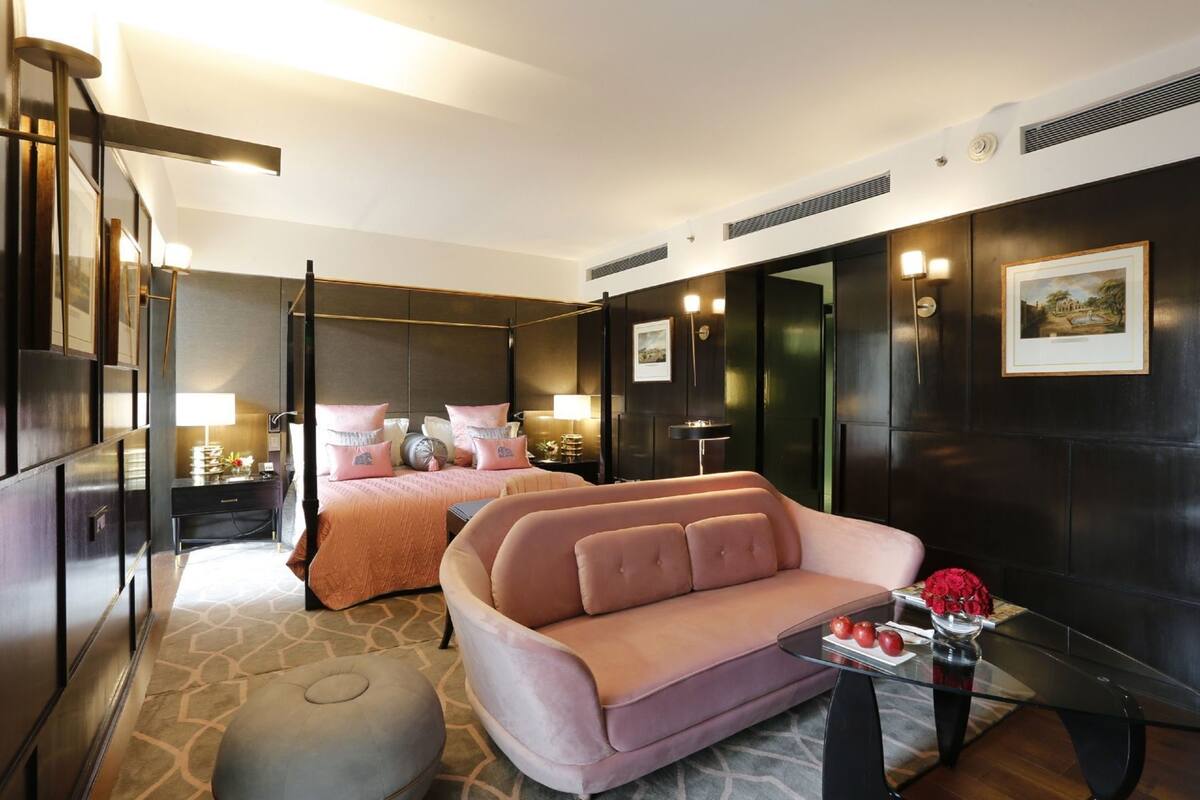A modern hotel room with a bed, a sofa, a glass coffee table, and a small side table with a vase of flowers.
