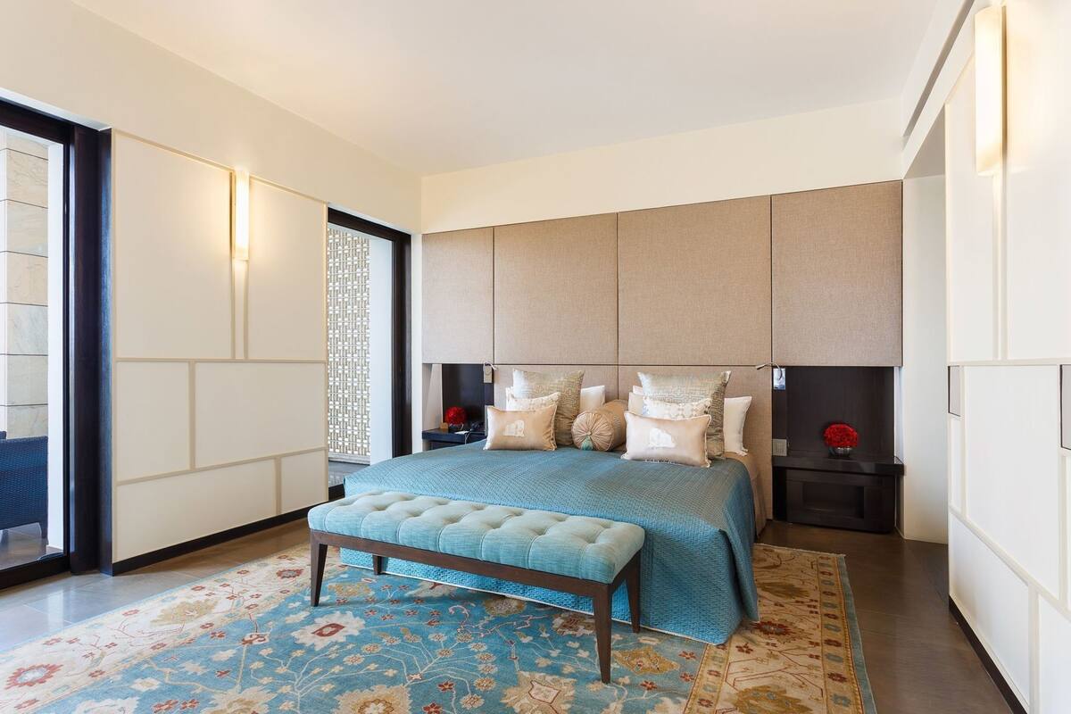 A modern bedroom with a large bed, a bench, a nightstand, and a decorative wall panel.