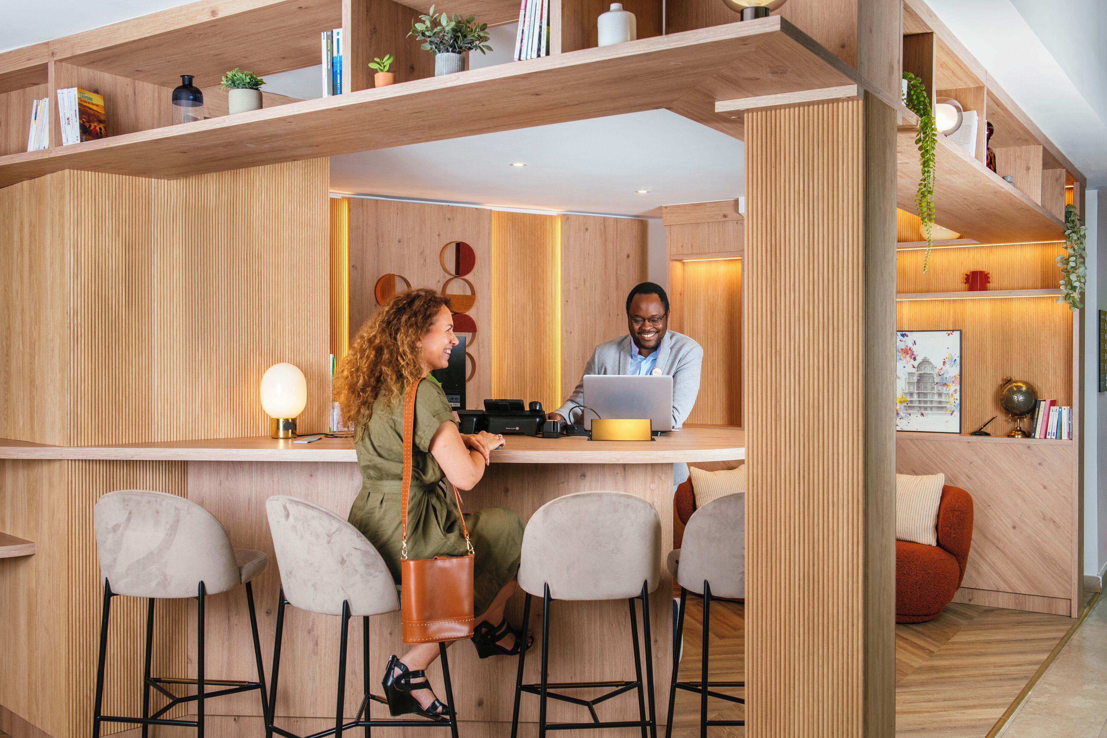 A modern reception area with wooden paneling, a counter, bar stools, and a seating area with a cushioned chair.