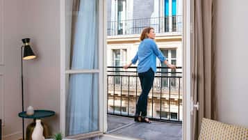 Une pièce dotée d’une grande porte-fenêtre coulissante donnant sur un balcon, d’une petite table ronde avec un vase et un livre, et d’un lampadaire.