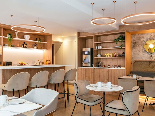 A modern kitchen with a built-in coffee machine, wooden shelves, and a round dining table with chairs. - Aparthotel Adagio Paris Opéra (Paris)